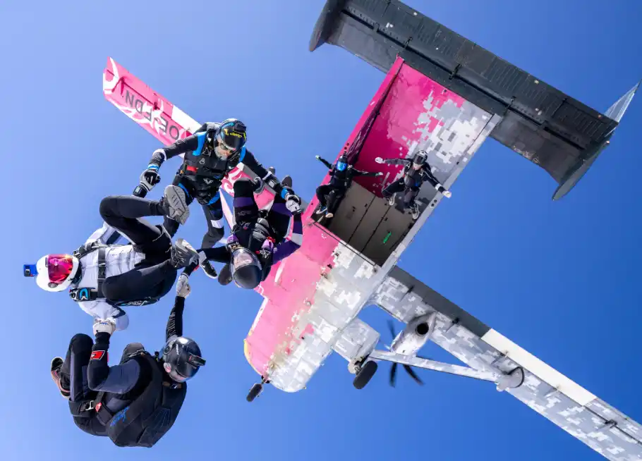 Three skydivers flying in formation above the clouds at sunset